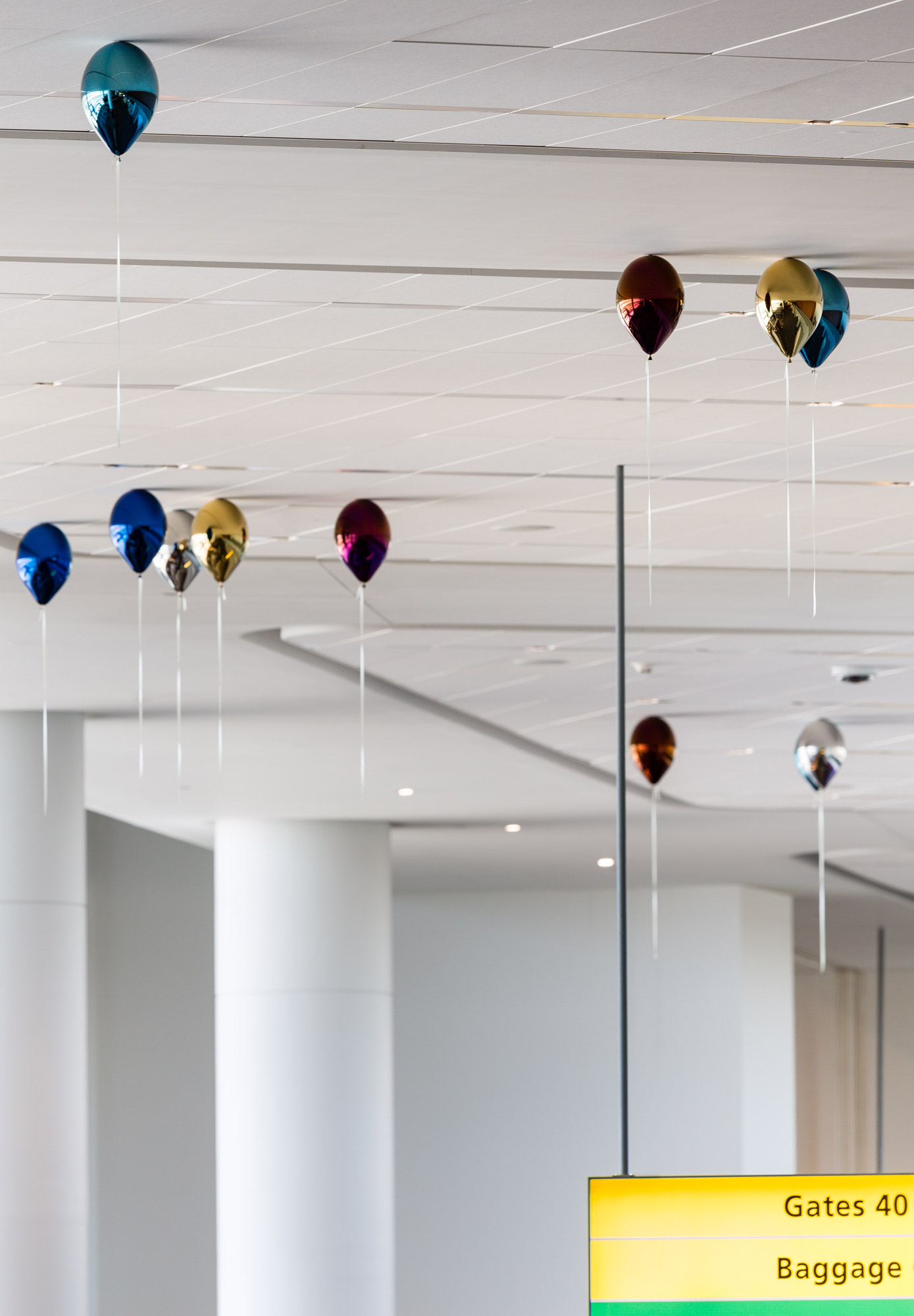 A series of metallic balloons appear to float against a white ceiling. The balloons are in blue, silver, green, magenta, red, and gold.