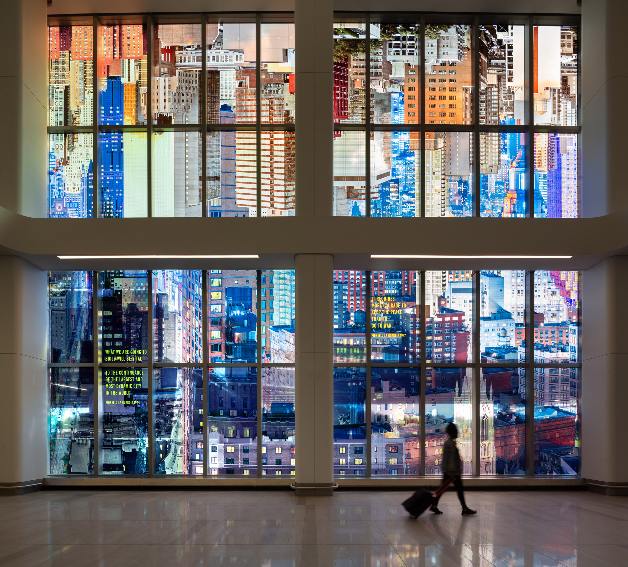 A kaleidoscopic wash of a colorful photo-collaged cityscape fills the length of two stories of tall glass windows in an airport terminal interior.