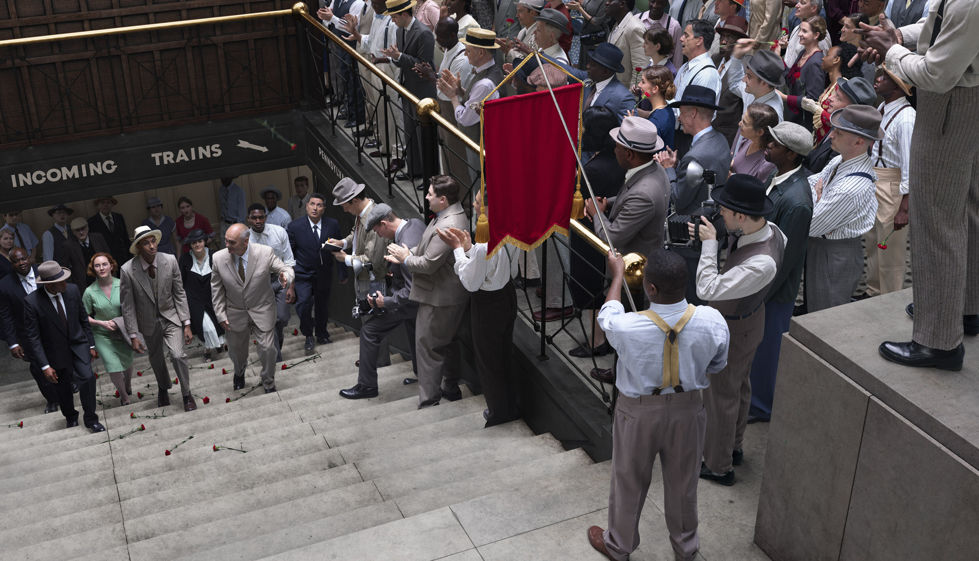 People dressed in winter fashions from the 1920s gather around the stairs to observe and photograph the emergence of an arrested woman.