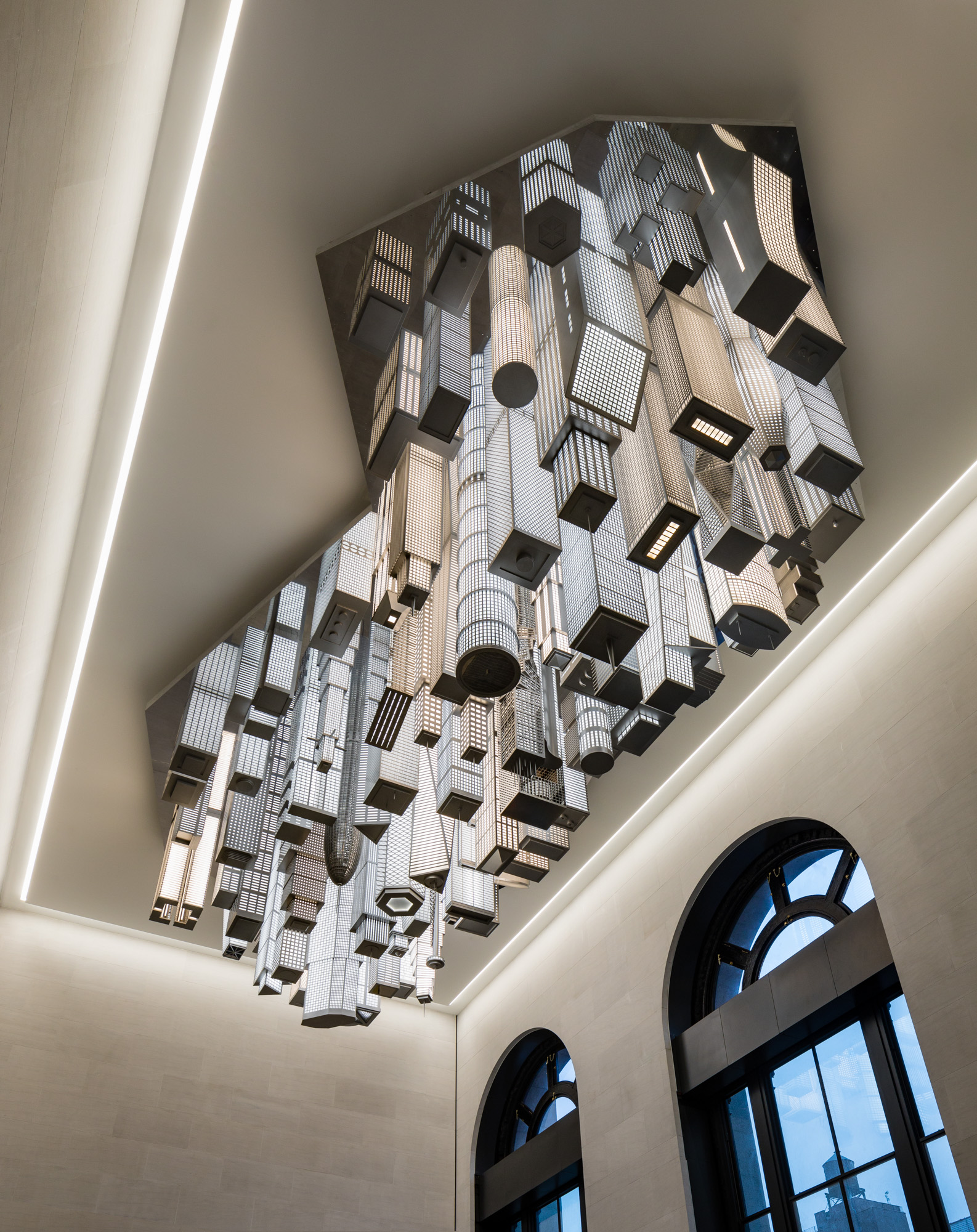 A crop of black and white lit up high-rise buildings descending from the ceiling of the interior of a train station.