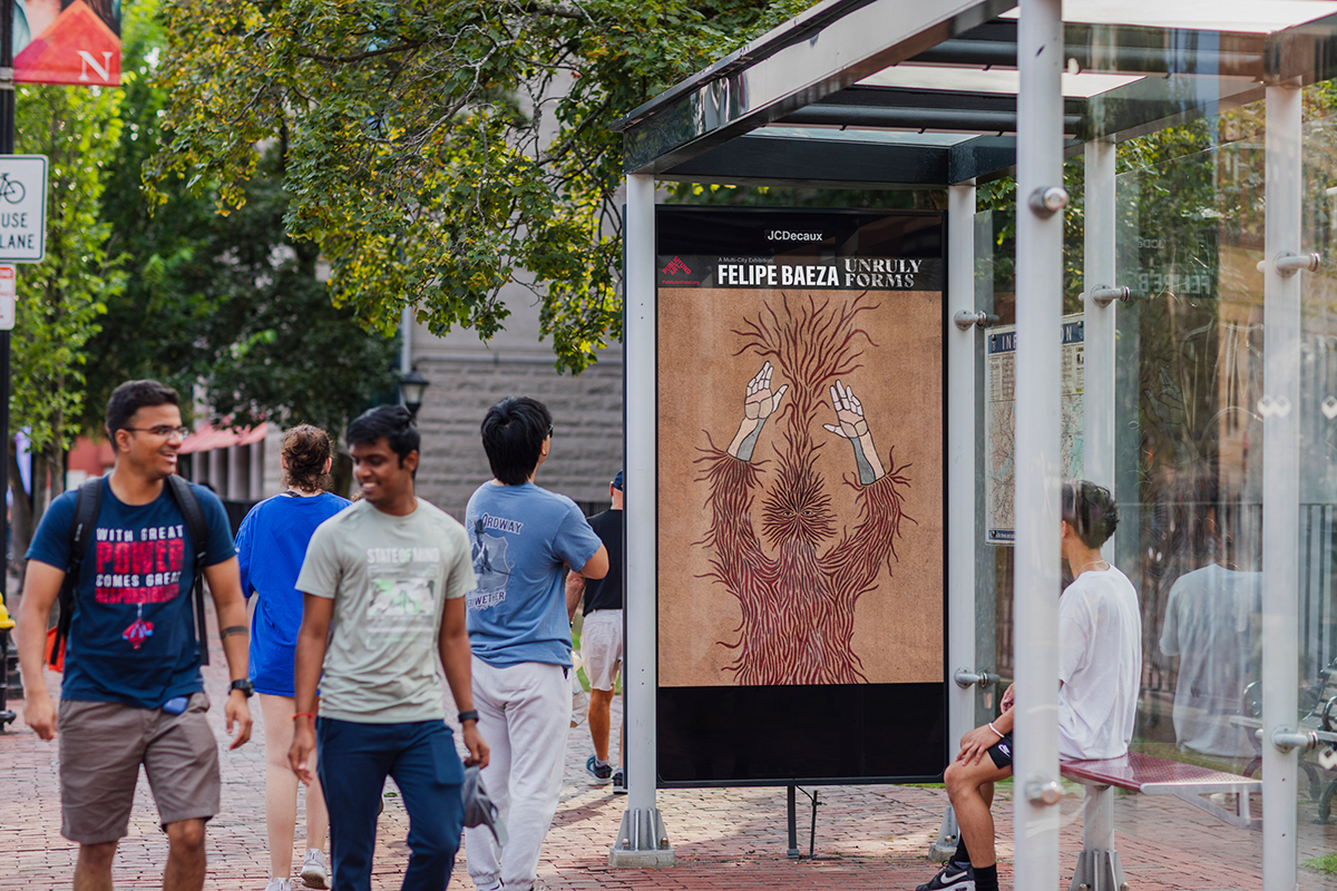 Pictured on a bus shelter on a busy city street is a layered hybrid figure that merges human, artifact, animal, and vegetation. The figure is composed of small...