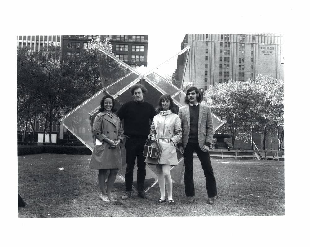 A black and white photograph of two women and two men standing in front of a large geometric sculpture in a park.
