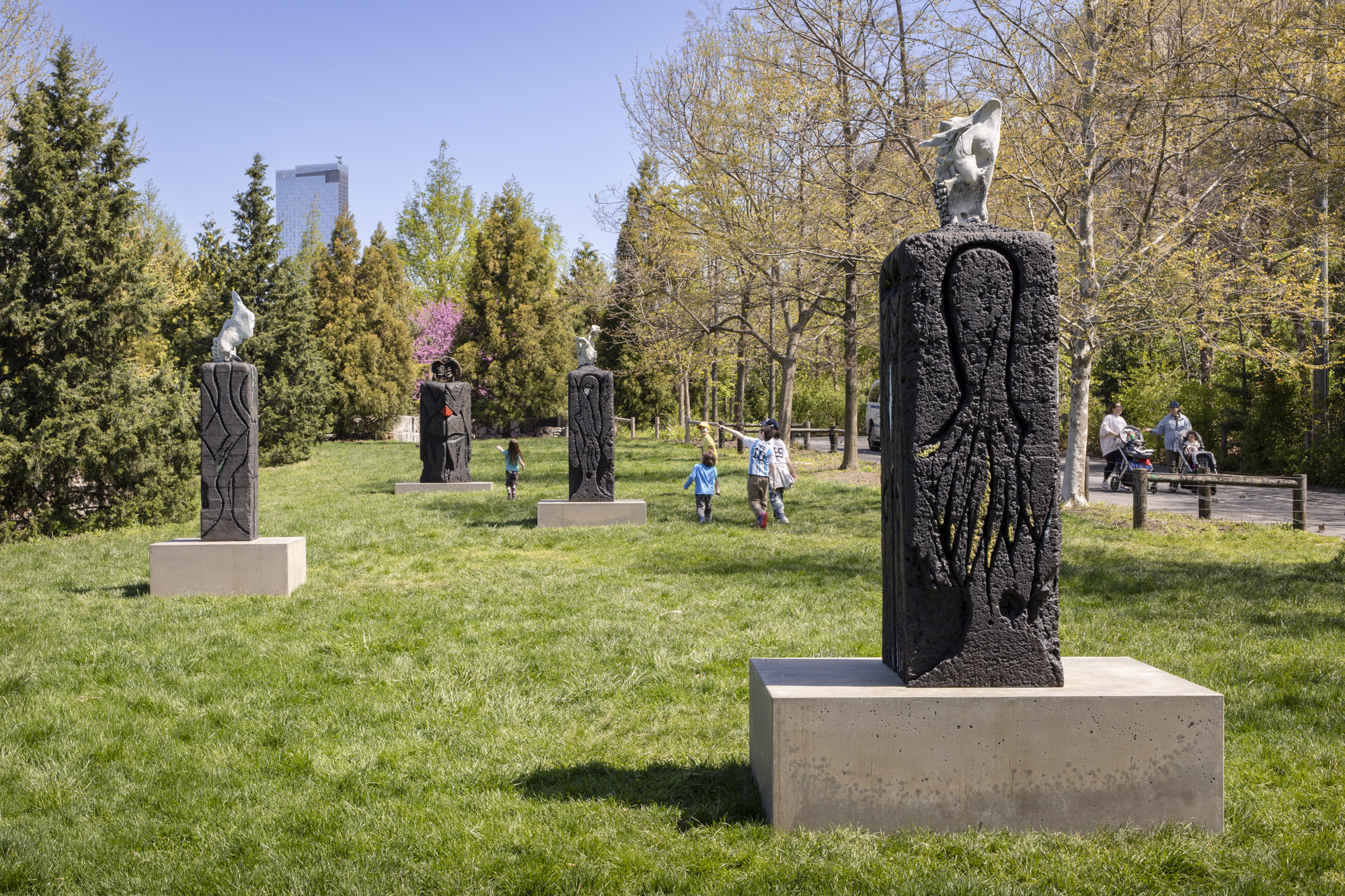 Four patinated bronze sculptures, each with a square concrete base, installed along a grassy terrace. On top of each sculpture sits a recreated skeletal structure:...