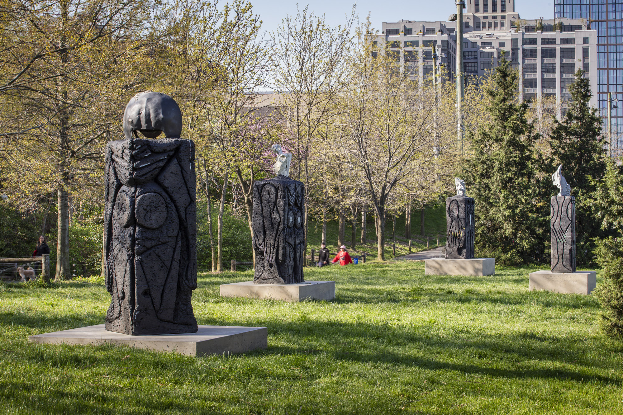 Four patinated bronze sculptures, each with a square concrete base, installed along a grassy terrace. On top of each sculpture sits a recreated skeletal structure:...