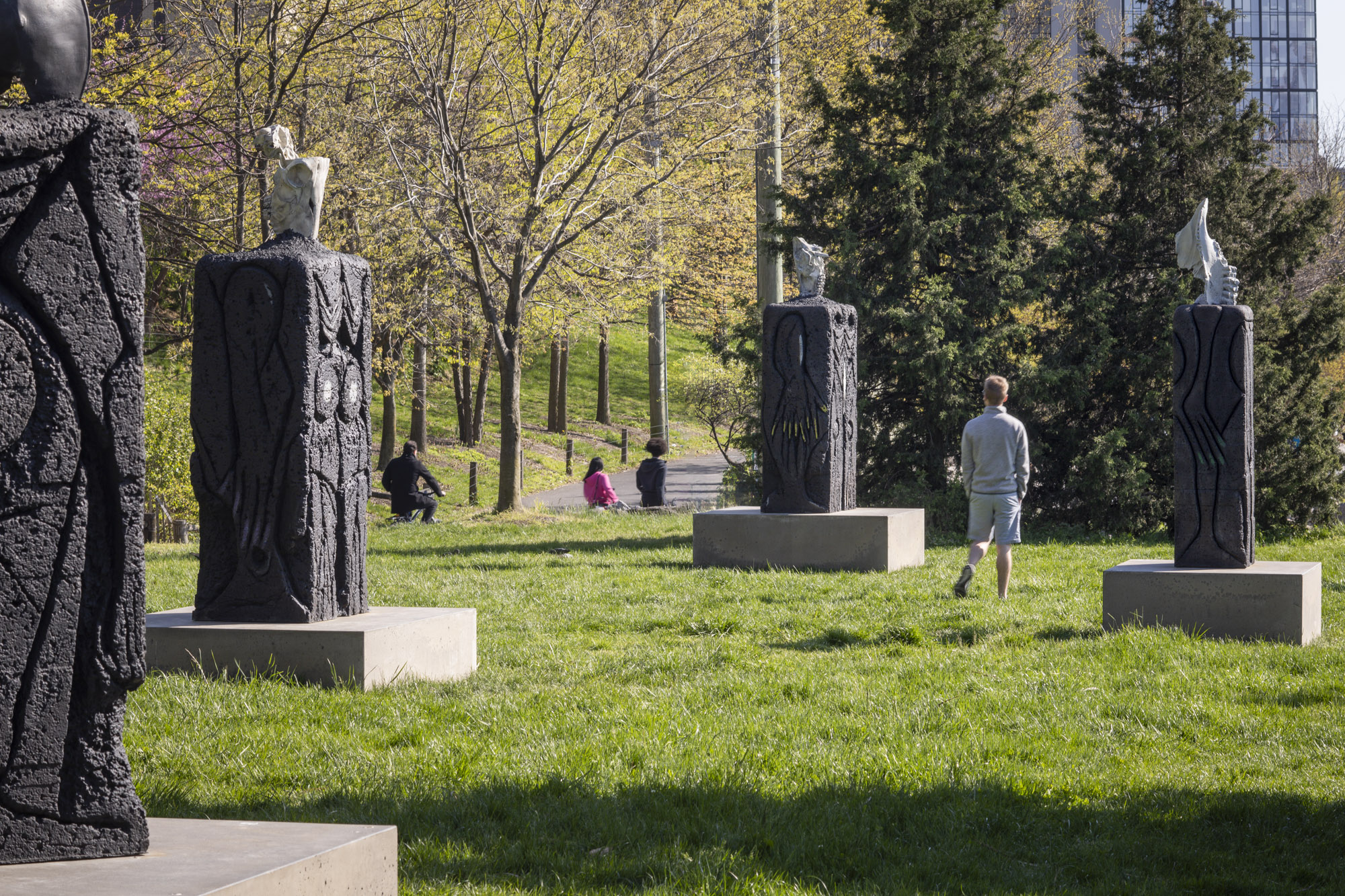 Four patinated bronze sculptures, each with a square concrete base, installed along a grassy terrace. On top of each sculpture sits a recreated skeletal structure:...